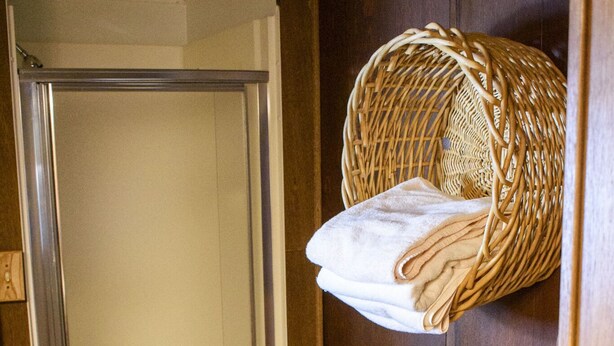 Une pièce en bois avec une douche, un panier en osier contenant des serviettes, une petite table avec une bougie et un panier tressé.