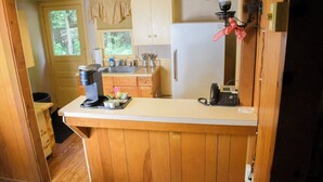 Une cuisine compacte avec des meubles de rangement en bois, un réfrigérateur, une machine à café et un petit évier.