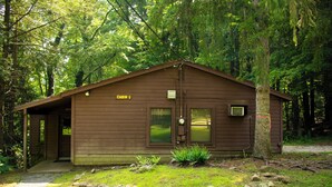 Une cabane portant l’inscription « CABANE 1 », dotée d’une porte, de fenêtres et d’un petit espace porche.