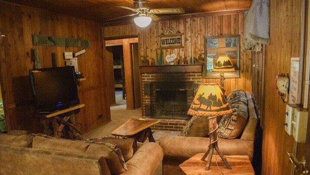 Ein gemütliches Blockhaus-Interieur mit Kamin, Ledersofas, Fernseher und einem 'Welcome'-Schild.