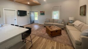 Amplia sala de estar con techo alto, techo de madera, sofá color beige, mesa de centro y televisor montado en la pared.