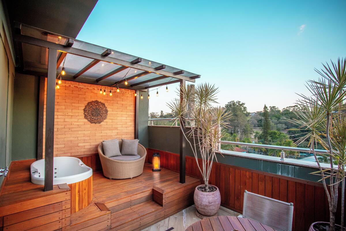 Een houten terras met een jacuzzi, rieten meubels en potplanten.