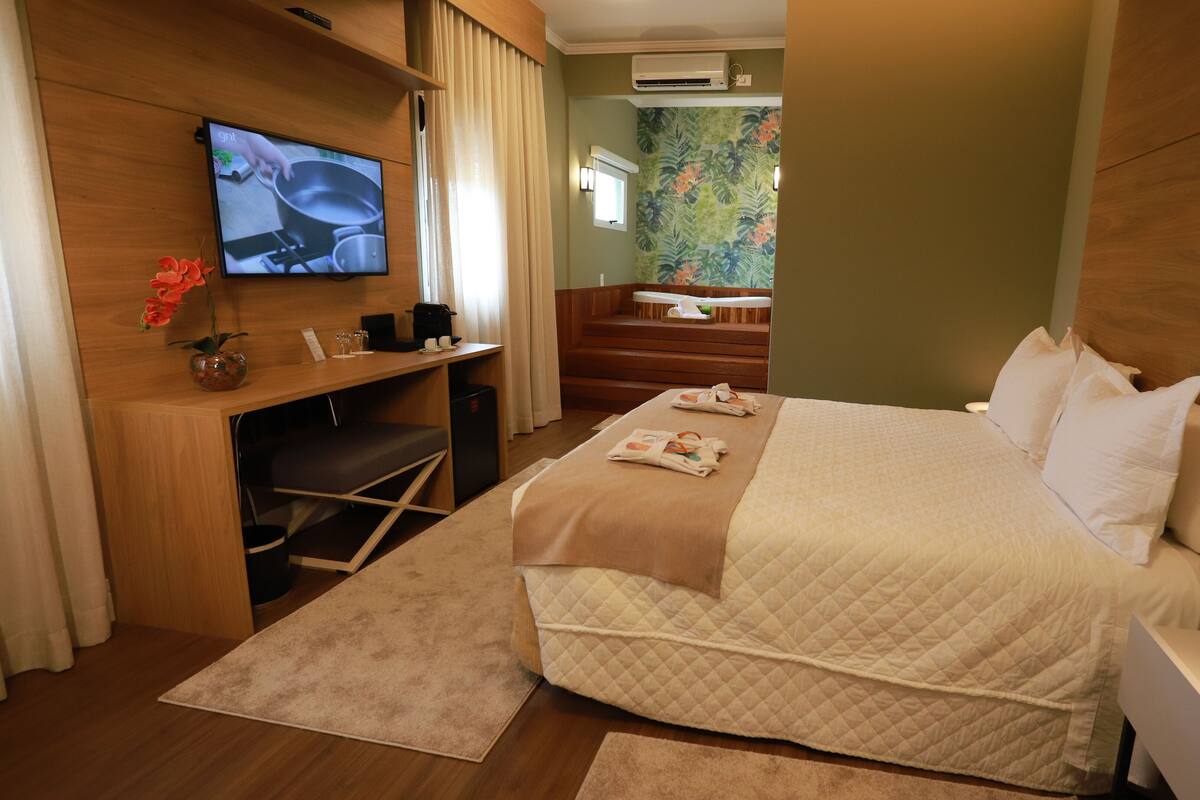 Een hotelkamer met een bed, een bureau met televisie, een kleine koelkast en een plant.