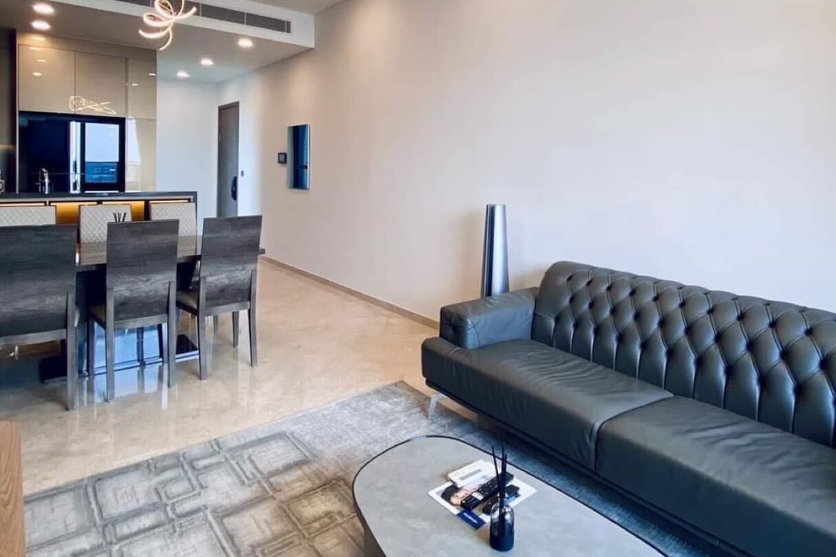 Una sala de estar moderna con un sofá gris, una zona de comedor con una mesa y sillas, y una cocina al fondo.