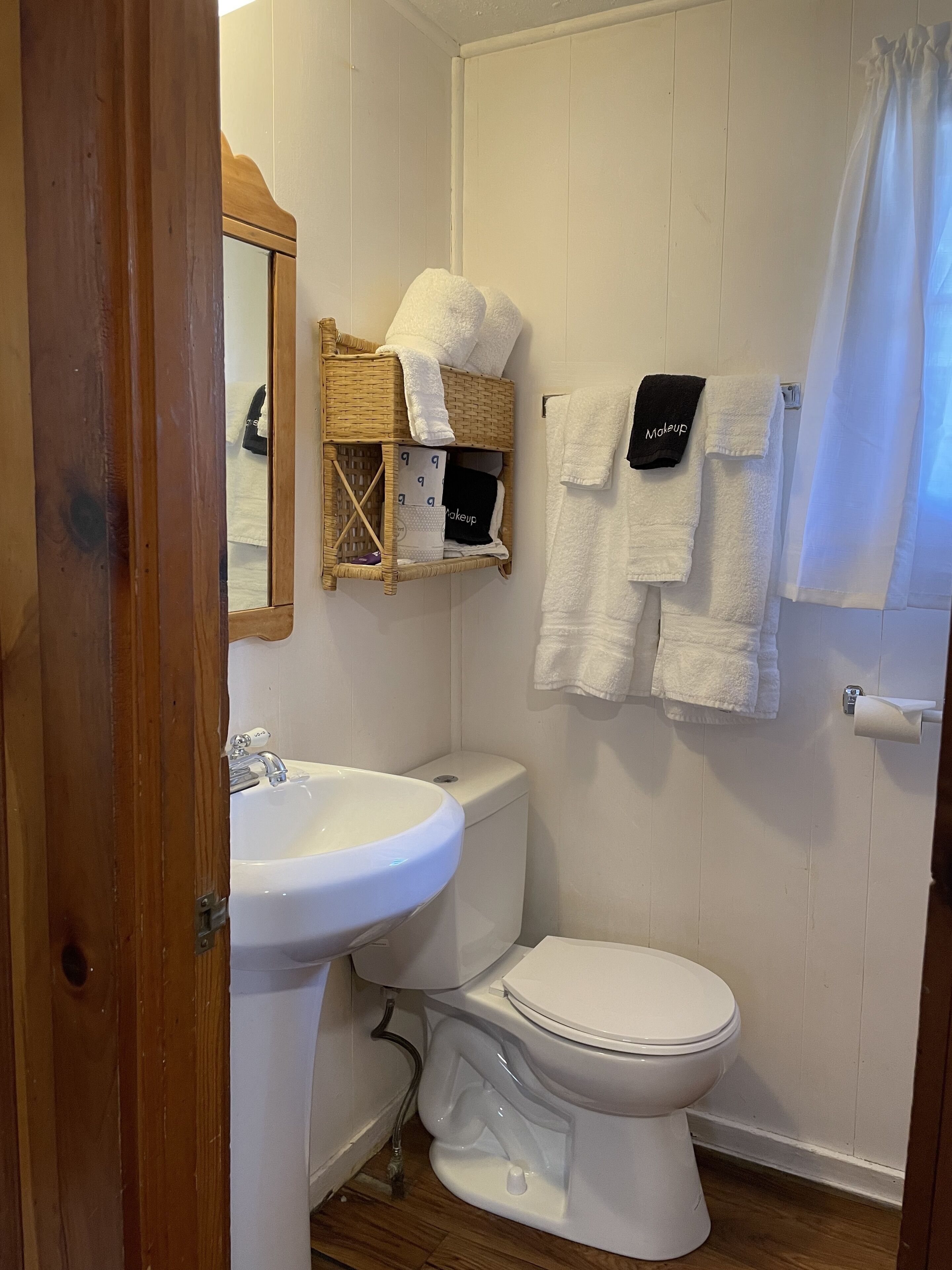 Un baño con lavamanos blanco, inodoro y una cesta de mimbre con toallas.