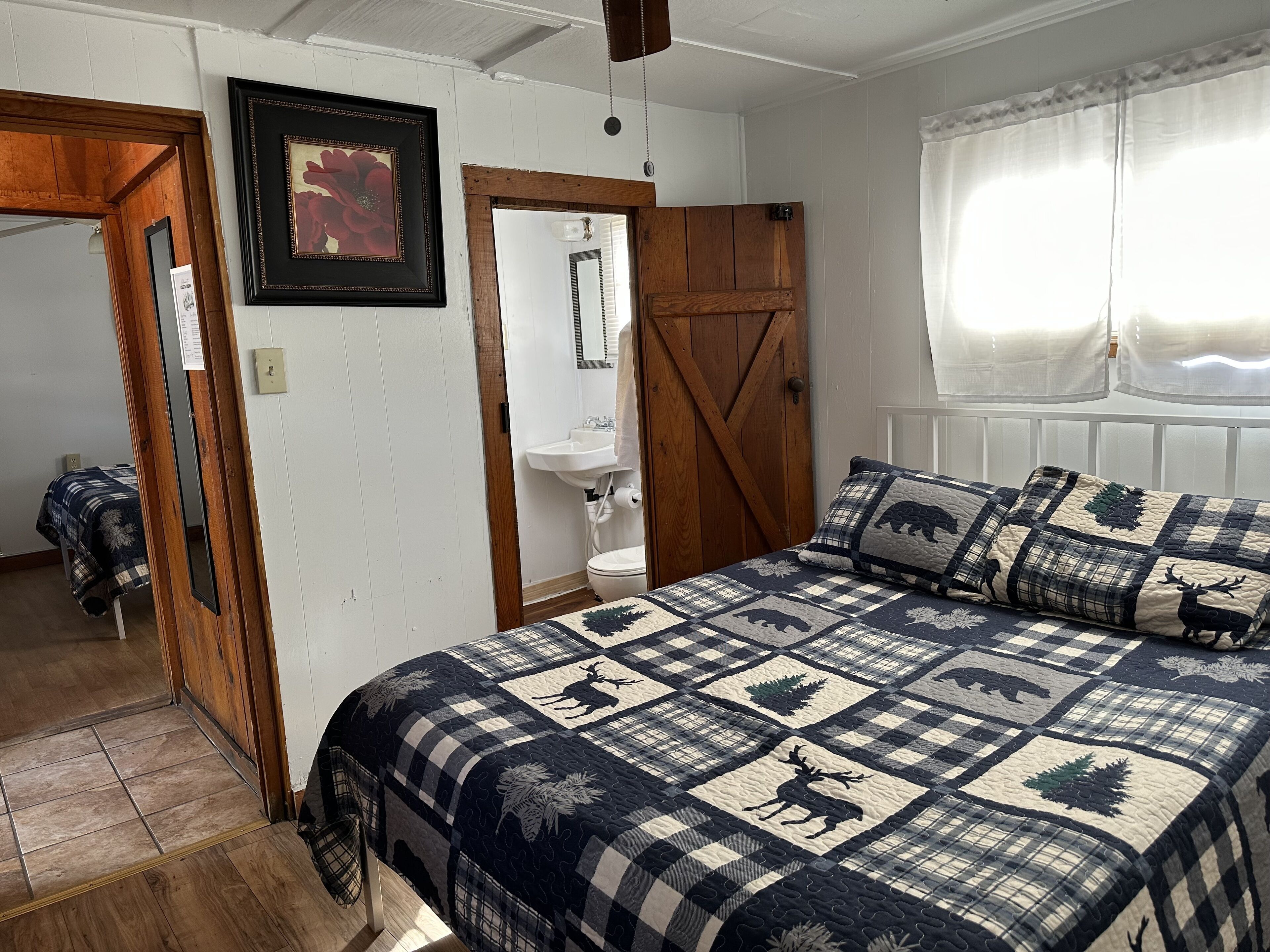 Un dormitorio con una cama grande, una puerta de madera, un lavamanos blanco y una ventana con cortinas de encaje.