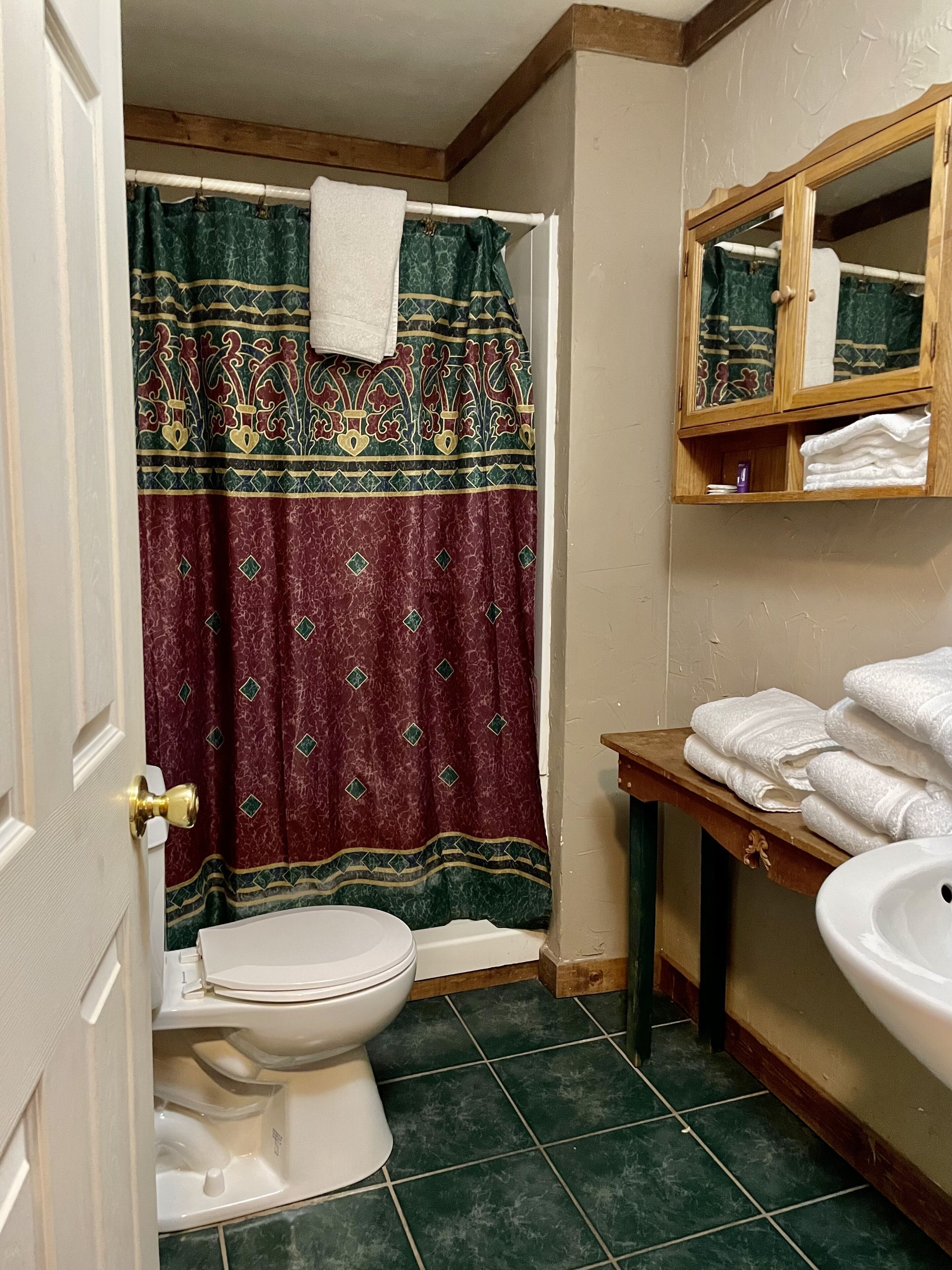 Un baño con inodoro, lavabo, tocador de madera, espejo y cortina de ducha.
