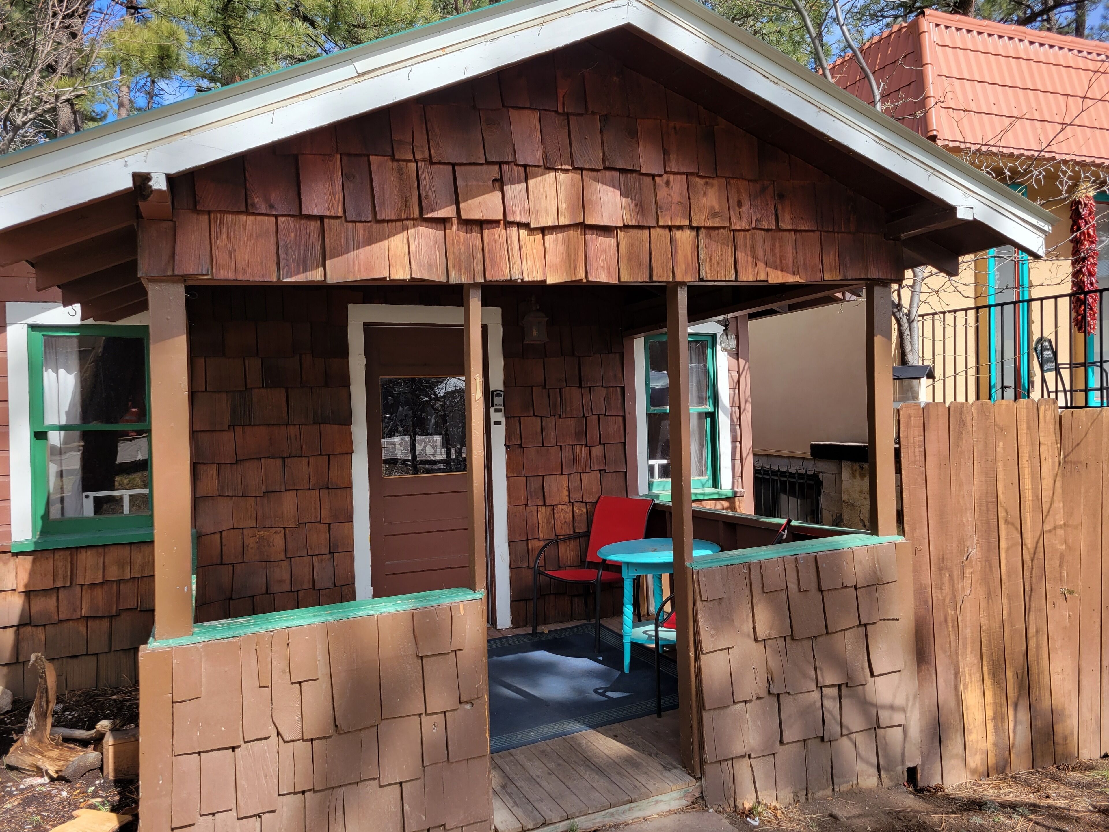 Une petite cabane en bois avec une véranda, une porte et une table entourée de chaises.