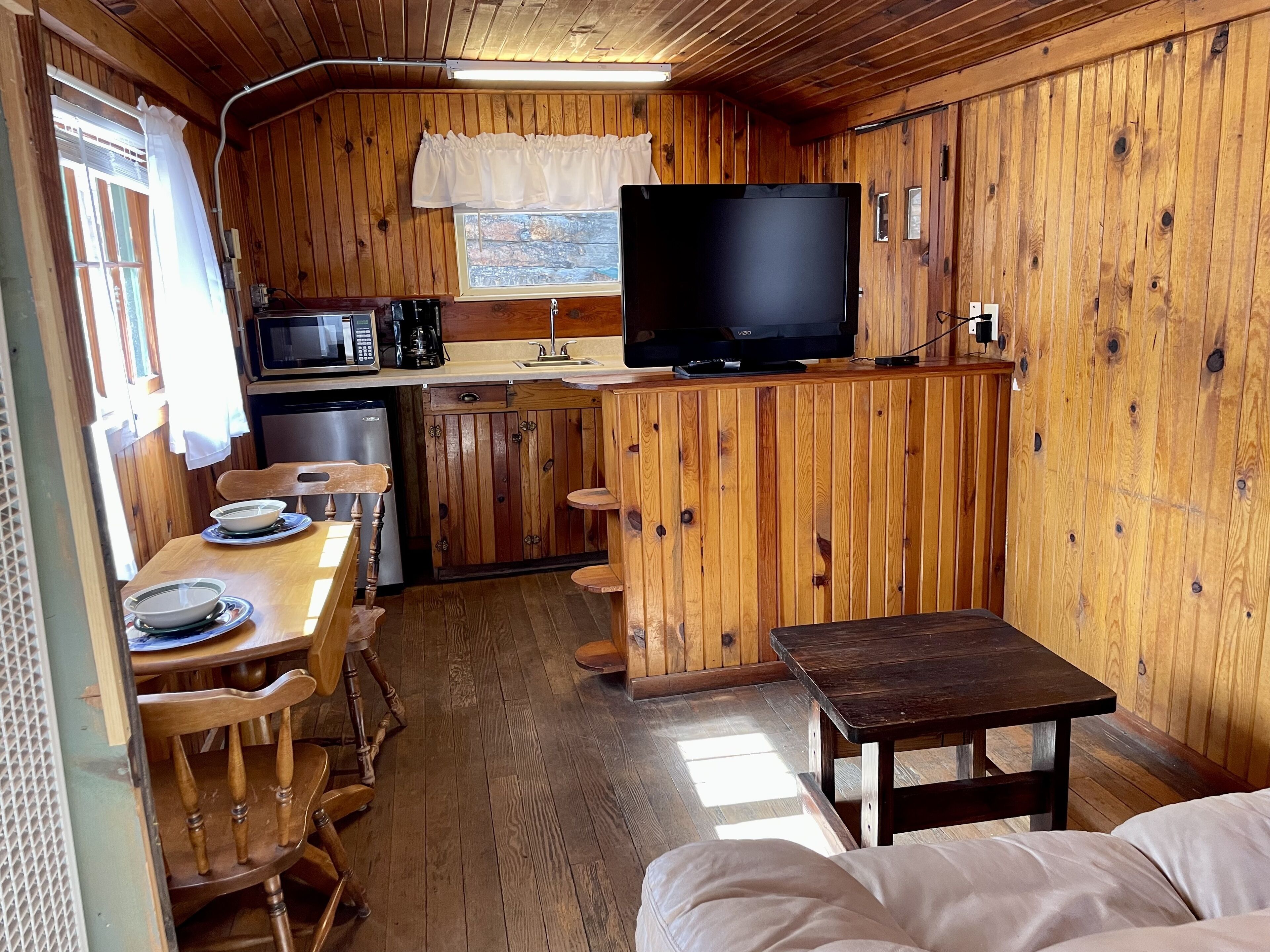 A compact kitchen with wooden walls, a microwave, a coffee maker, and a TV on a wooden counter.