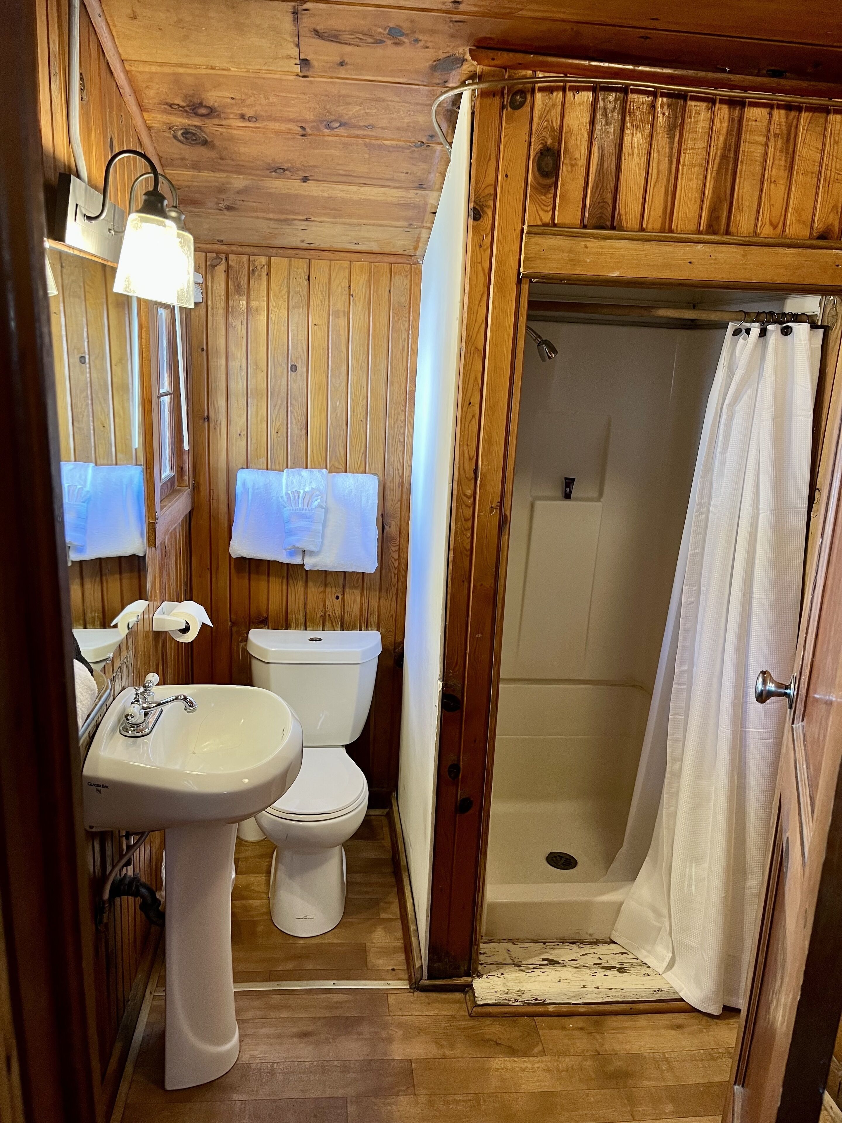 A wooden-paneled bathroom with a sink, toilet, and shower.