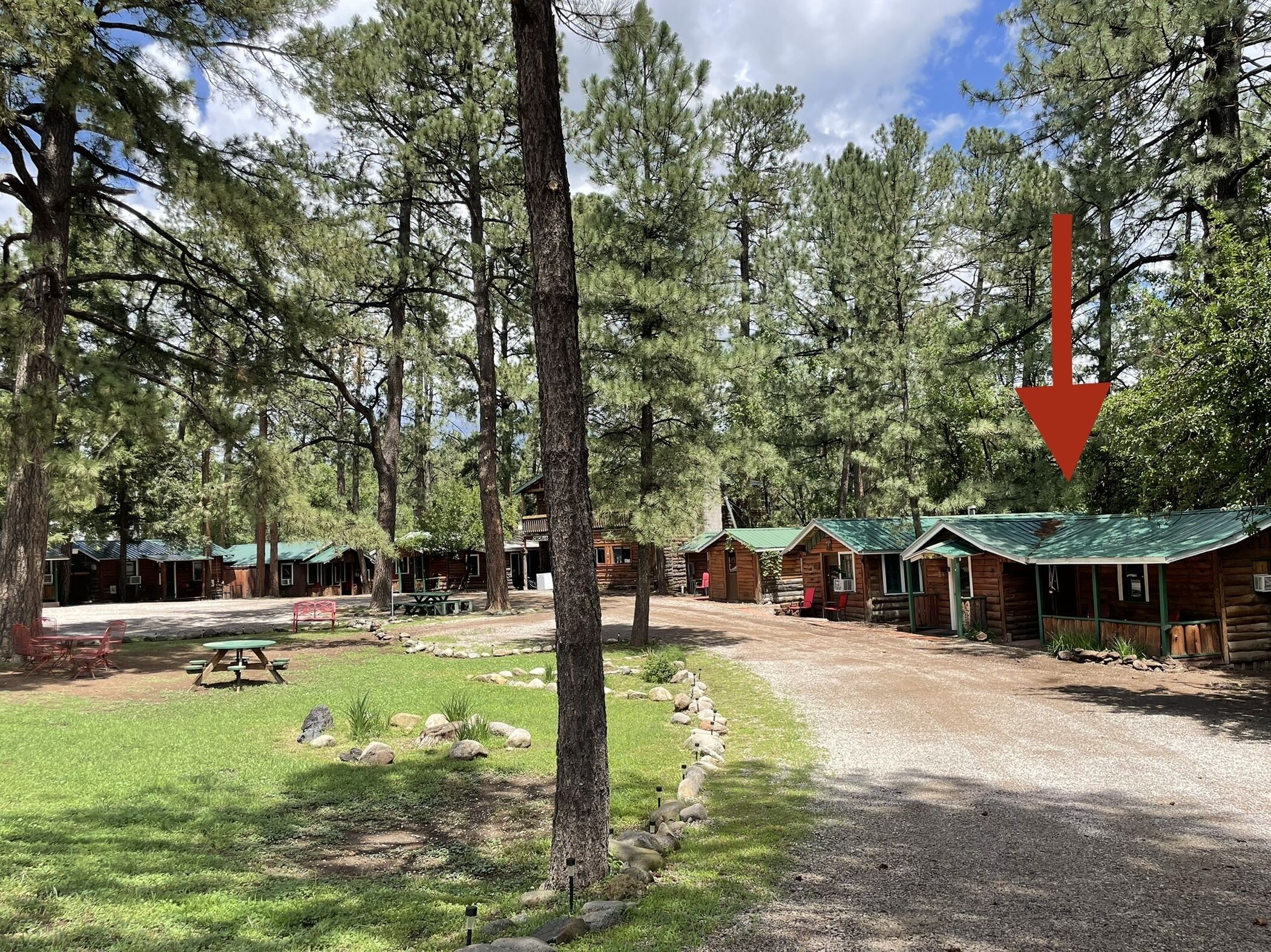 A campground with log cabins, picnic tables, and a gravel path.