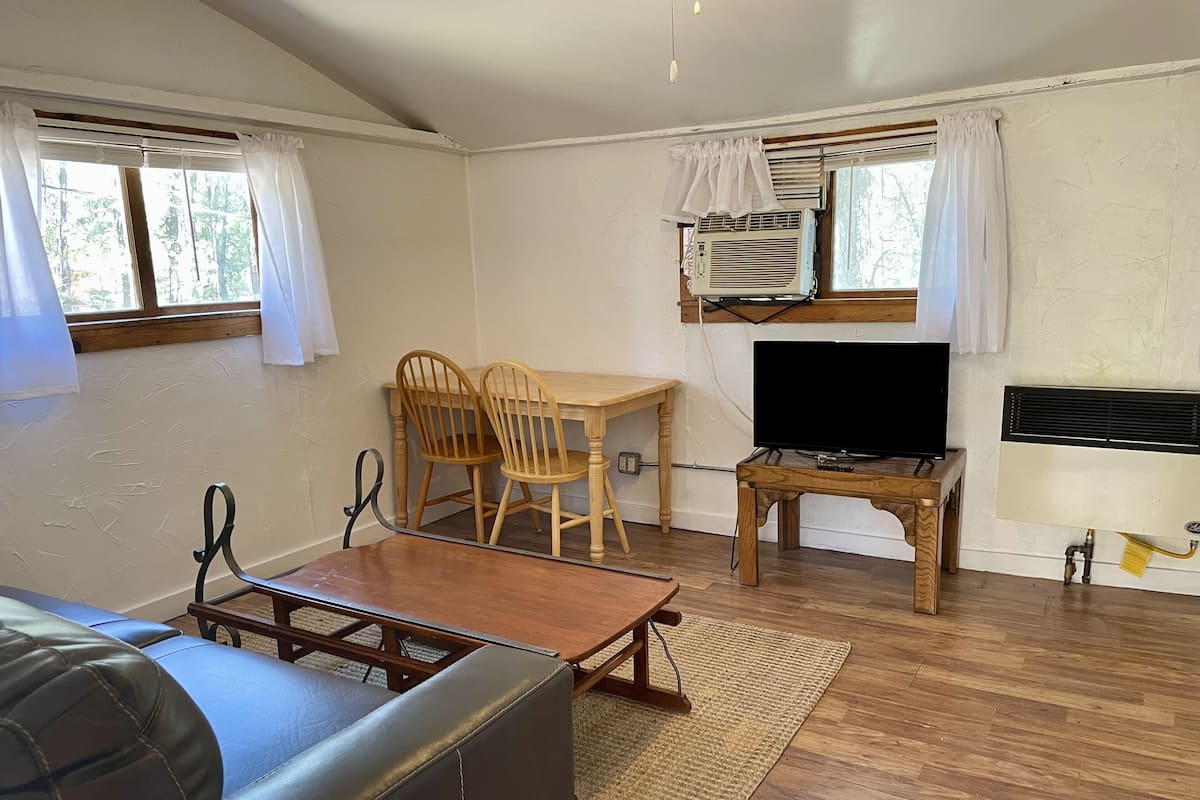 A room with a wooden table, two chairs, a television, and a sofa.