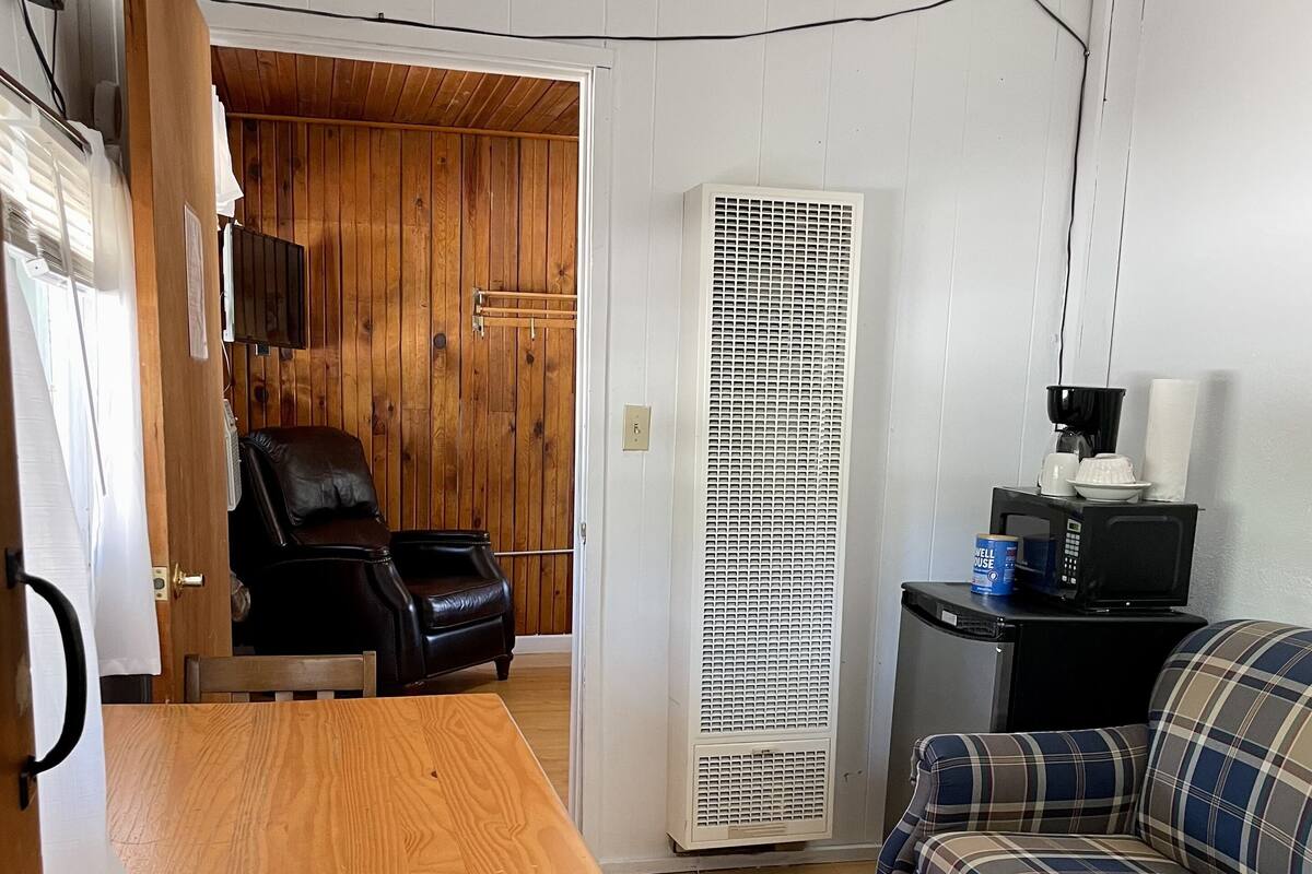 A room with a wooden table, a plaid sofa, a black leather chair, and a white air conditioning unit.