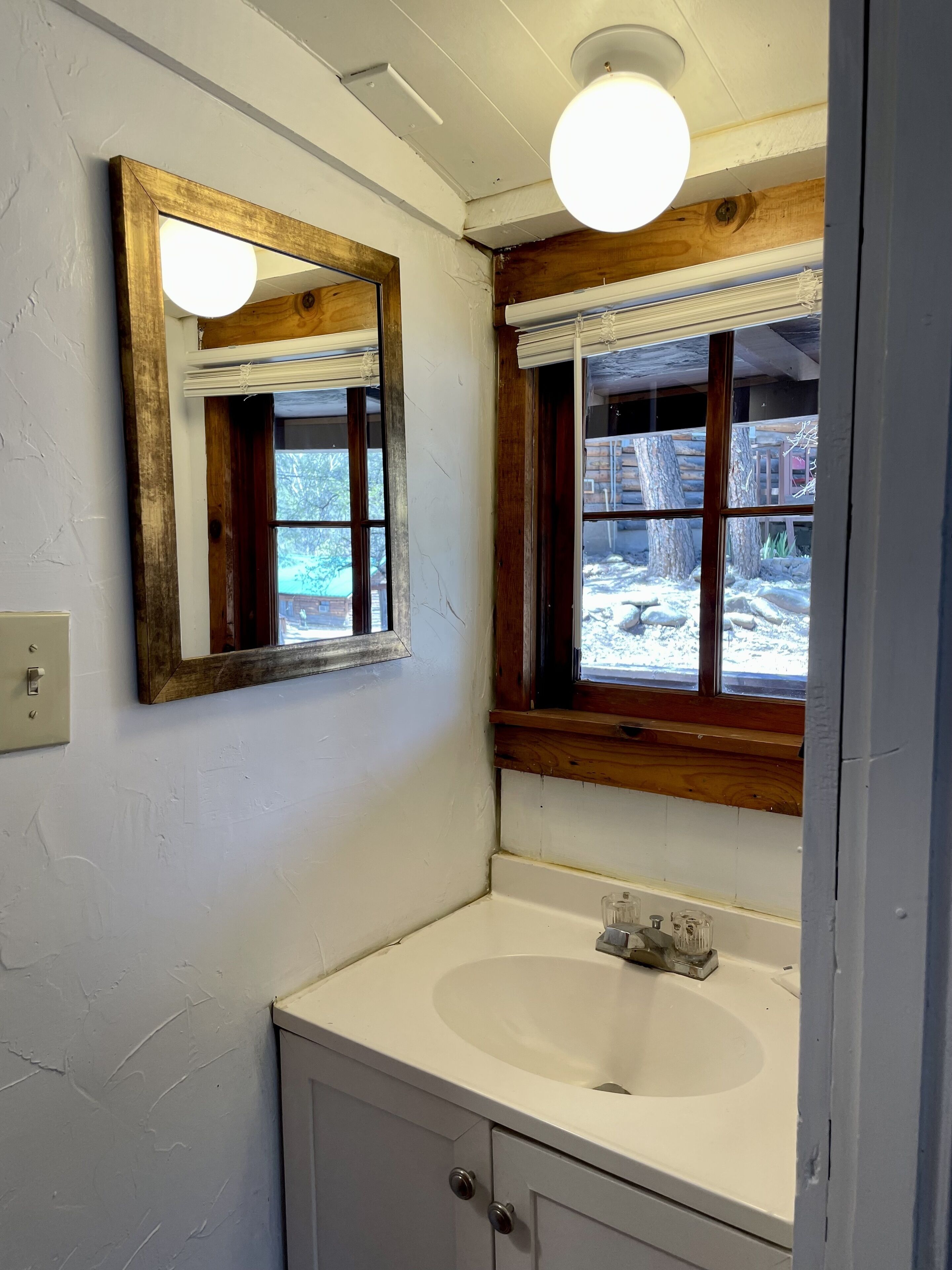 A bathroom with a white sink, wooden-framed mirror, and a window with a view of a snowy outdoor area.