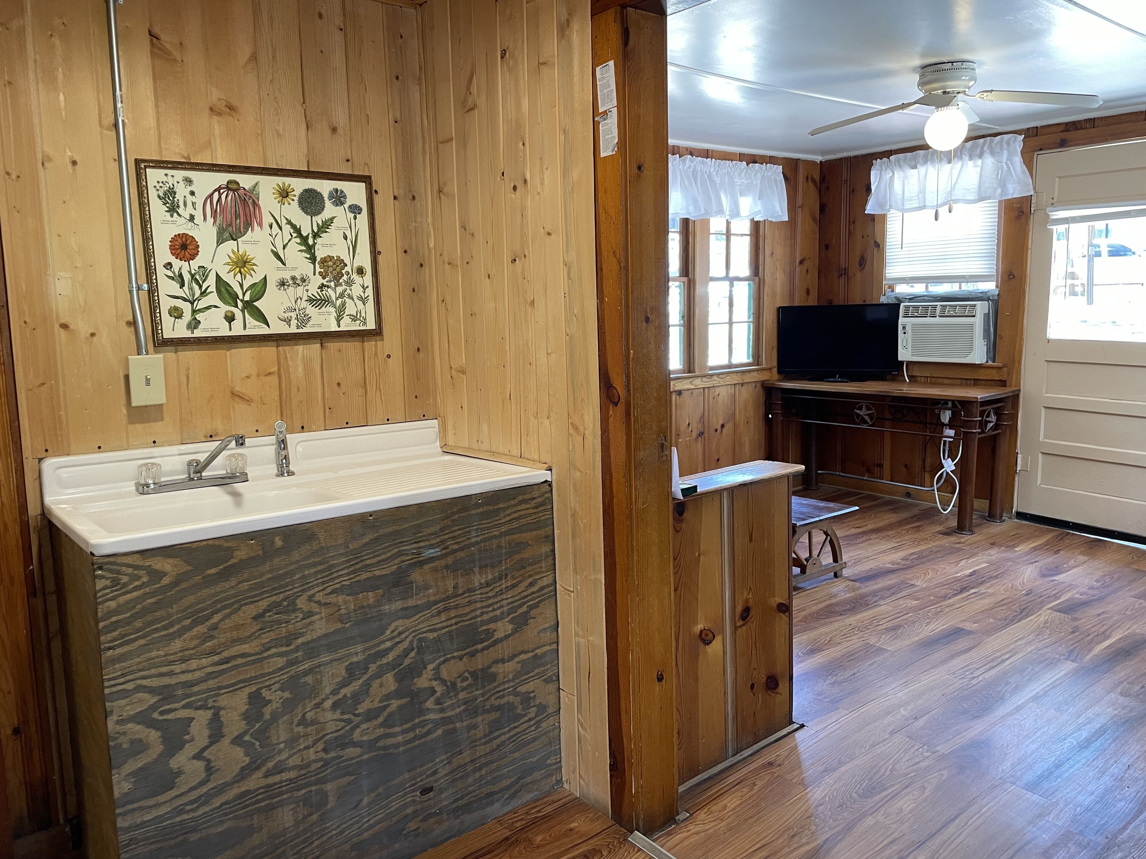 A wooden interior with a sink, a ceiling fan, and a television.