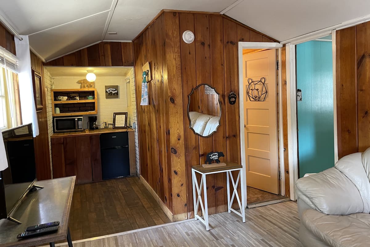 A compact cabin with a kitchenette, a small dining table, a sofa, and a mirror.