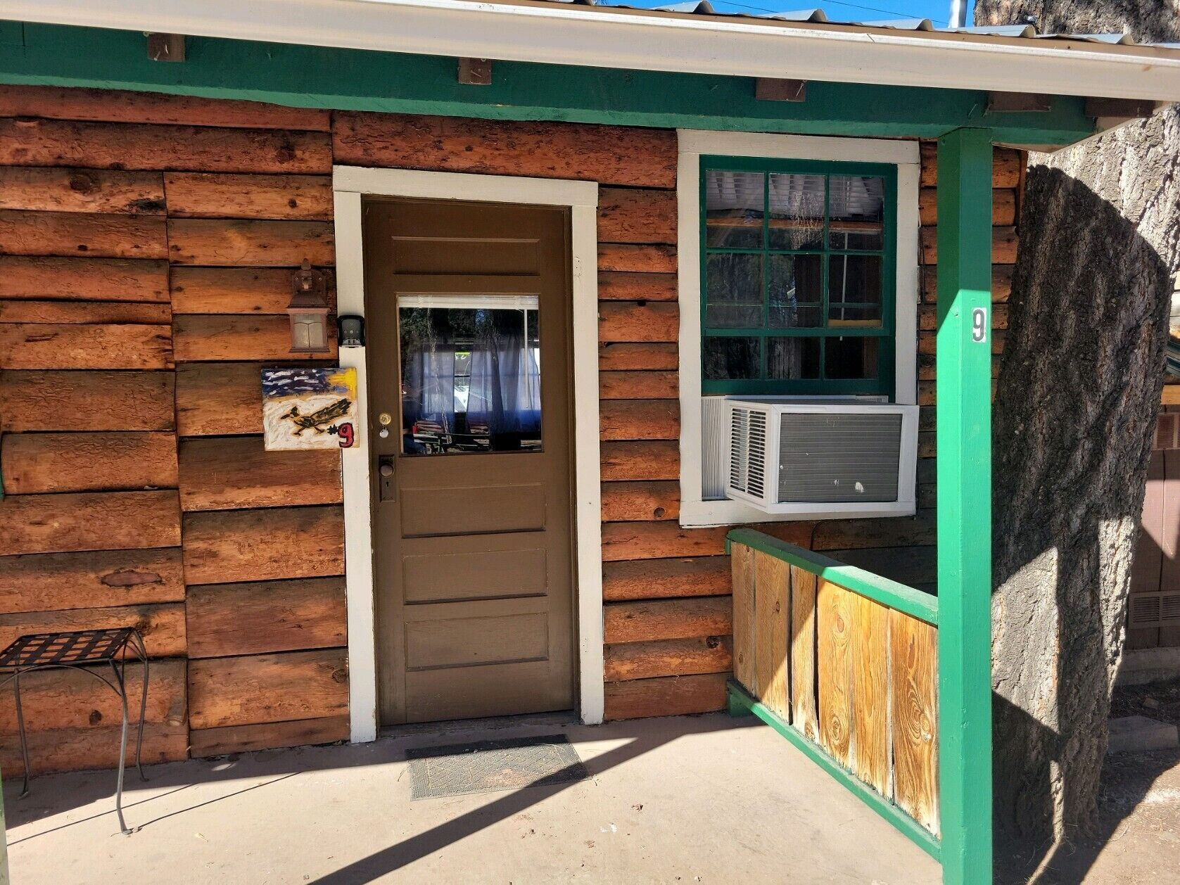 A wooden cabin with a brown door, a window with a green frame, and an air conditioning unit mounted on the wall.