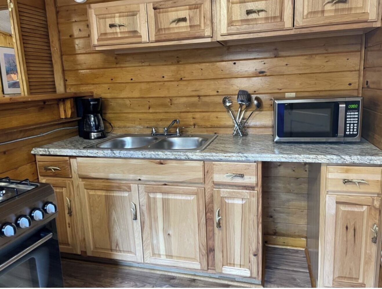 A kitchen with wooden cabinets, a double sink, a coffee maker, a microwave, and a gas stove.