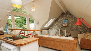A cozy loft-style room with a kitchen area, a dining table, and a large bed with a stone wall backdrop. - Tan y Craig (Haverfordwest)