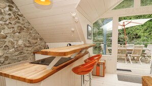 A kitchen with a wooden countertop, a built-in stove, and a stone wall. There is a window with a view of outdoor furniture. - Tan y Craig (Haverfordwest)