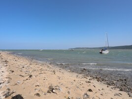 Una playa con un velero, costa rocosa y mar tranquilo.