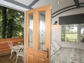 Una habitación con puerta de madera, una cama con ropa de cama floral, una silla blanca y una mesa con planta en maceta.