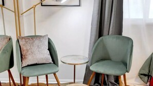 Una sala de estar moderna con dos sillones verdes, una mesa redonda de centro, una obra de arte con una planta enmarcada y una alfombra grande de fibras naturales.