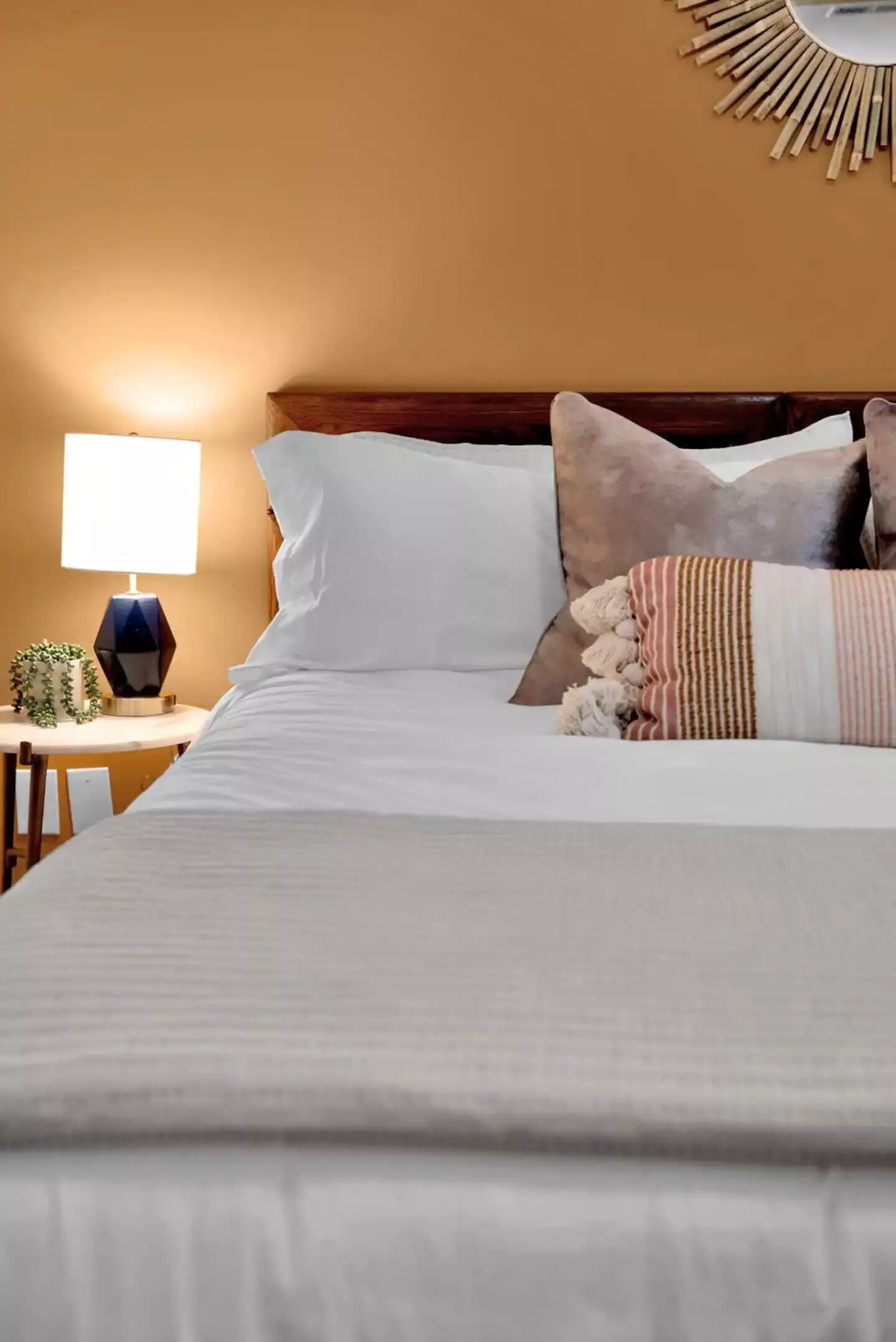 A neatly made bed with white linens, a wooden headboard, and decorative pillows.