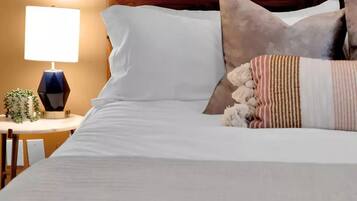 A neatly made bed with white linens, a wooden headboard, and decorative pillows.