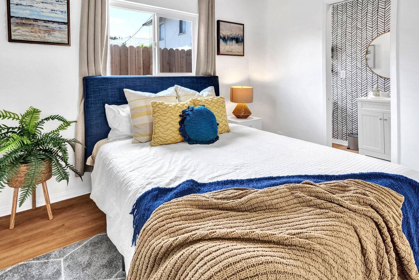 Un dormitorio con cama, una lámpara de noche, una planta en maceta y vistas al exterior.