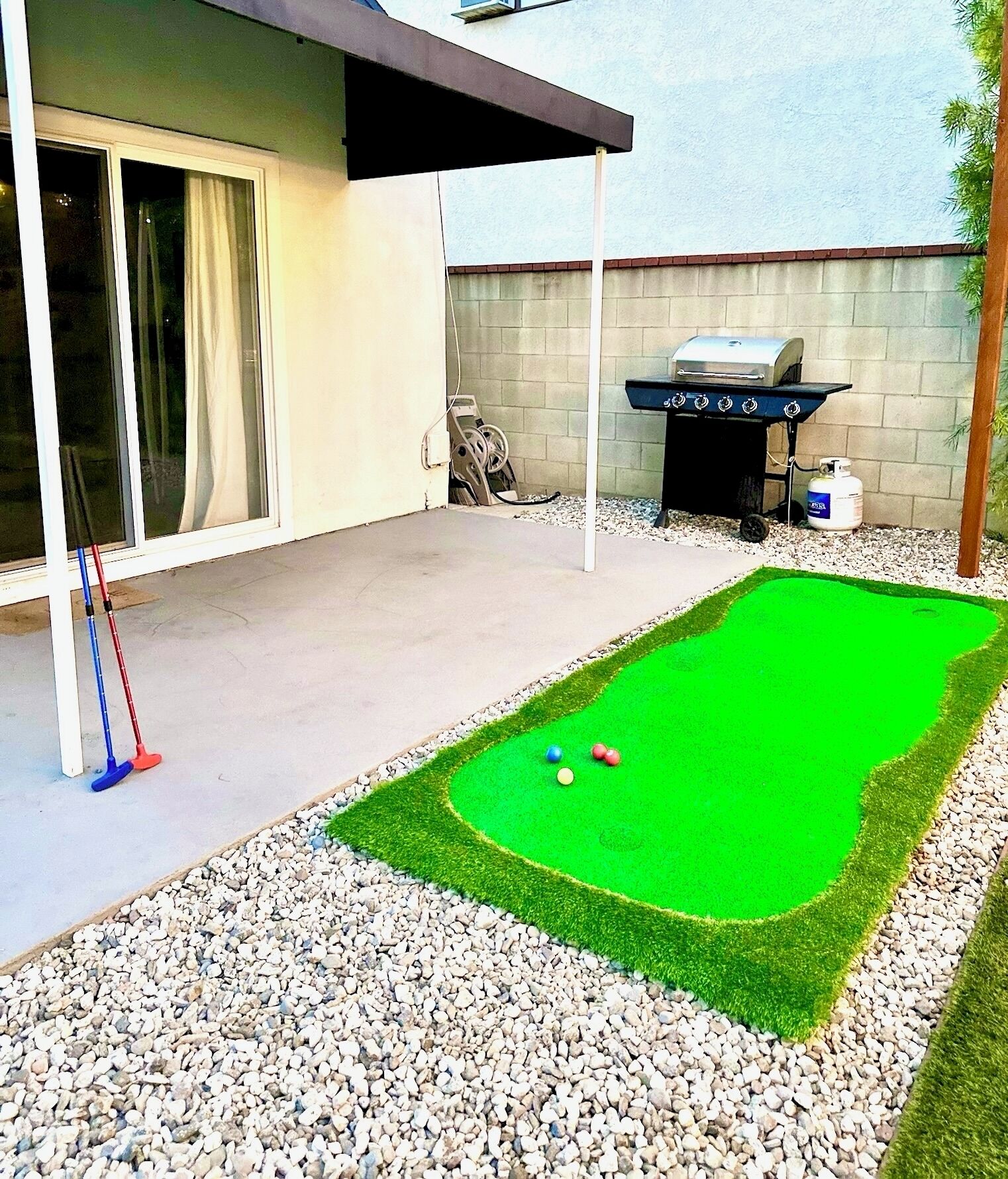 A backyard with a green lawn, a barbecue grill, and a pool table.