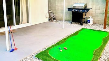 A backyard with a green lawn, a barbecue grill, and a pool table.