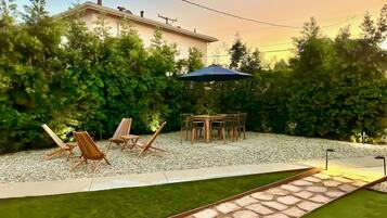 A backyard with a patio table and chairs, surrounded by a gravel area and a small water feature.