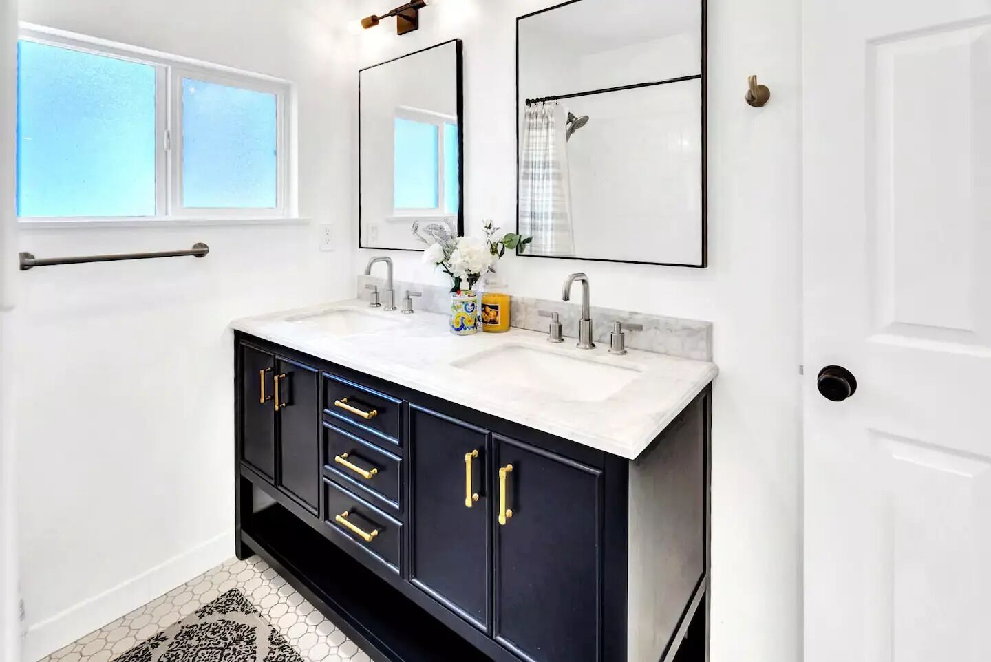 Une salle de bain avec un meuble-lavabo blanc, deux vasques, un grand miroir et une fenêtre.