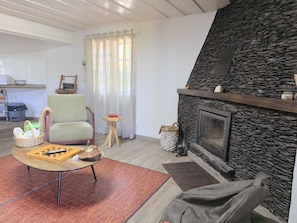 A living room with a stone fireplace, a green armchair, a coffee table with a puzzle, and a kitchen in the background.
