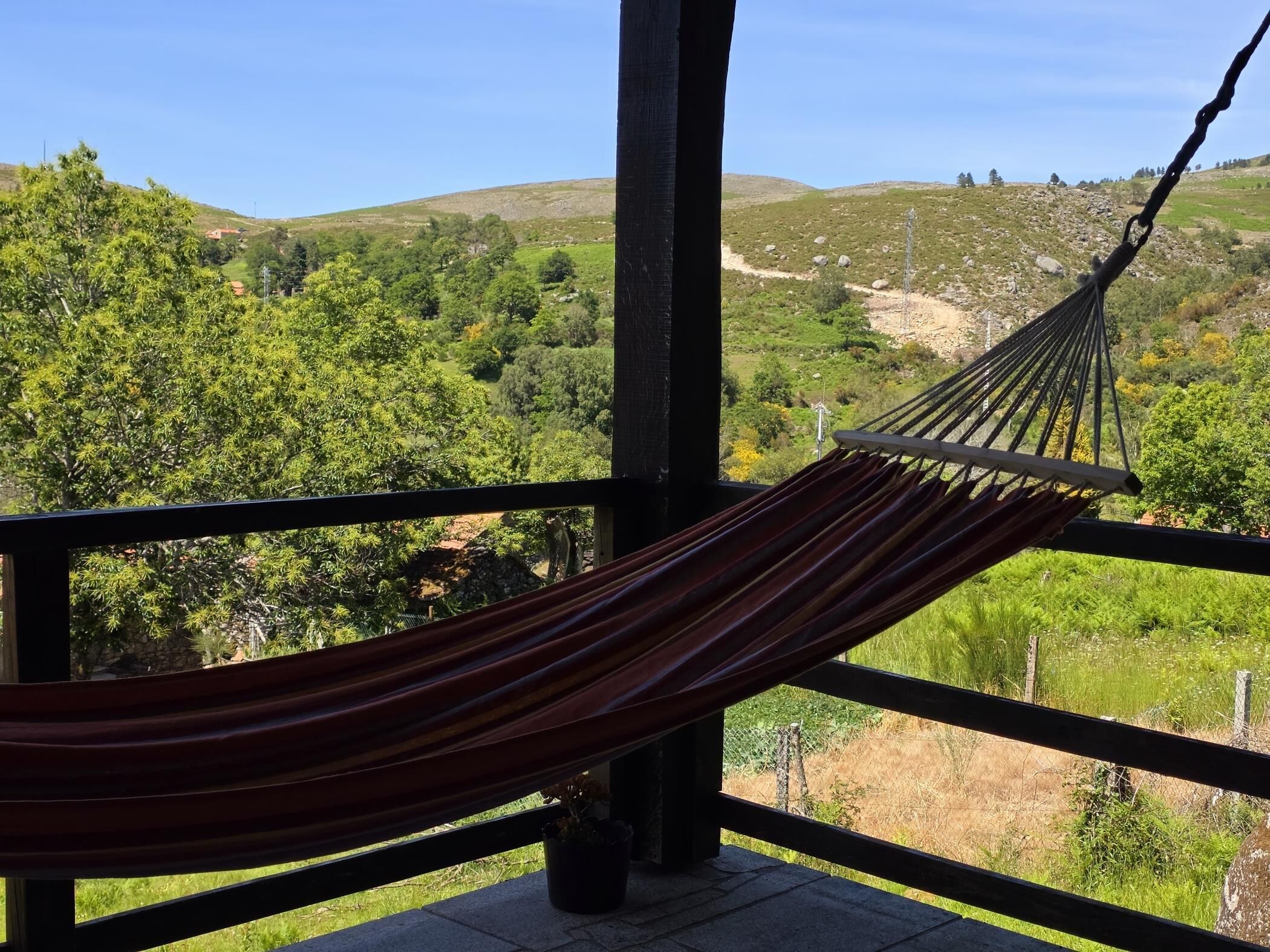 A hammock on a balcony with a view of a green landscape and hills.