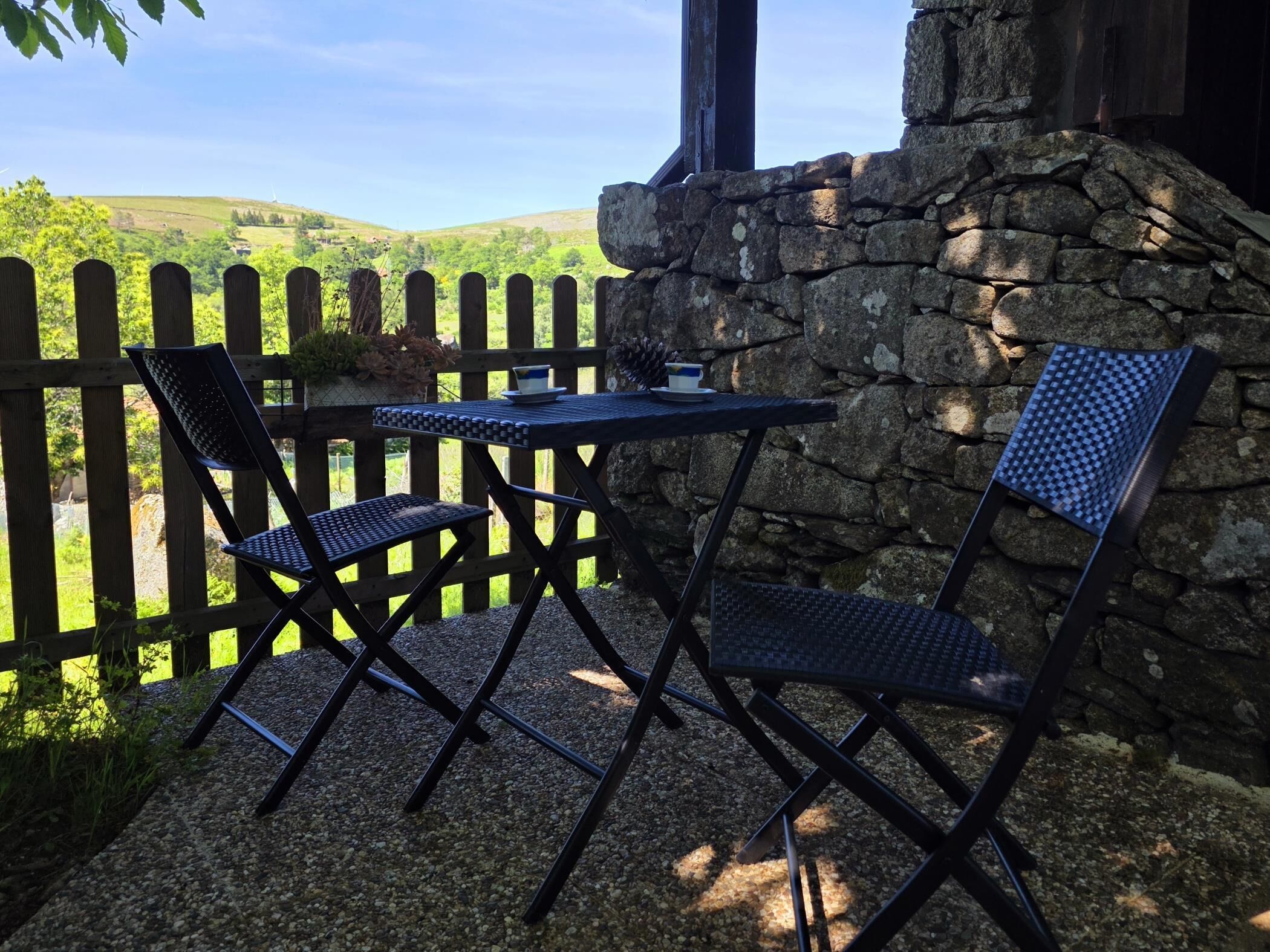 A patio with a stone wall, two chairs, and a table.
