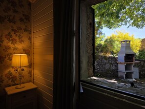 A room with a window overlooking a stone wall and a wood-burning stove.