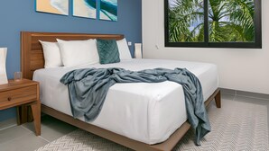 A bedroom with a bed, a nightstand, a ceiling fan, and a window with a view of palm trees. - Playa del Carmen (Playa del Carmen)