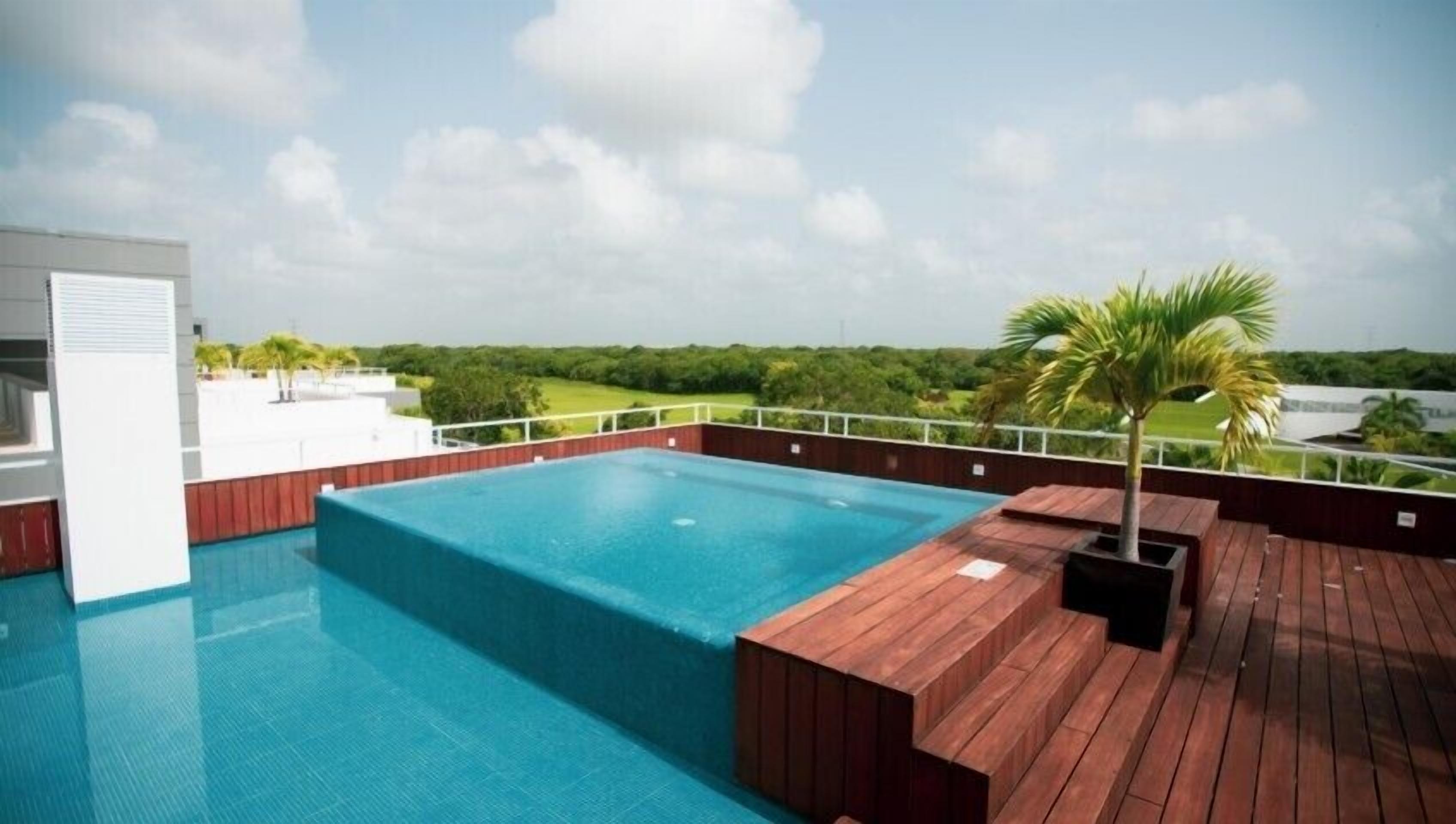 A rooftop swimming pool with a wooden deck and a view of a green landscape.