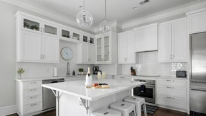 A modern kitchen with white cabinetry, a central island, bar stools, stainless steel appliances, and a clock on the wall. - Old Village | Amazing Location | The Big Spoon (Mt Pleasant)