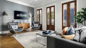 A modern living room with a grey sofa, two armchairs, a coffee table, and a flat-screen TV mounted on the wall. - Old Village | Amazing Location | The Big Spoon (Mt Pleasant)