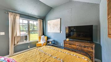 A bedroom with a bed, a TV, a dresser, and a window with curtains.