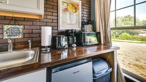 Een kleine keuken met een spoelbak, broodrooster, koffiezetapparaat en een Hisense magnetron. Daarboven hangt een lijst met bloemen, en op de muur staat een bordje met de tekst 