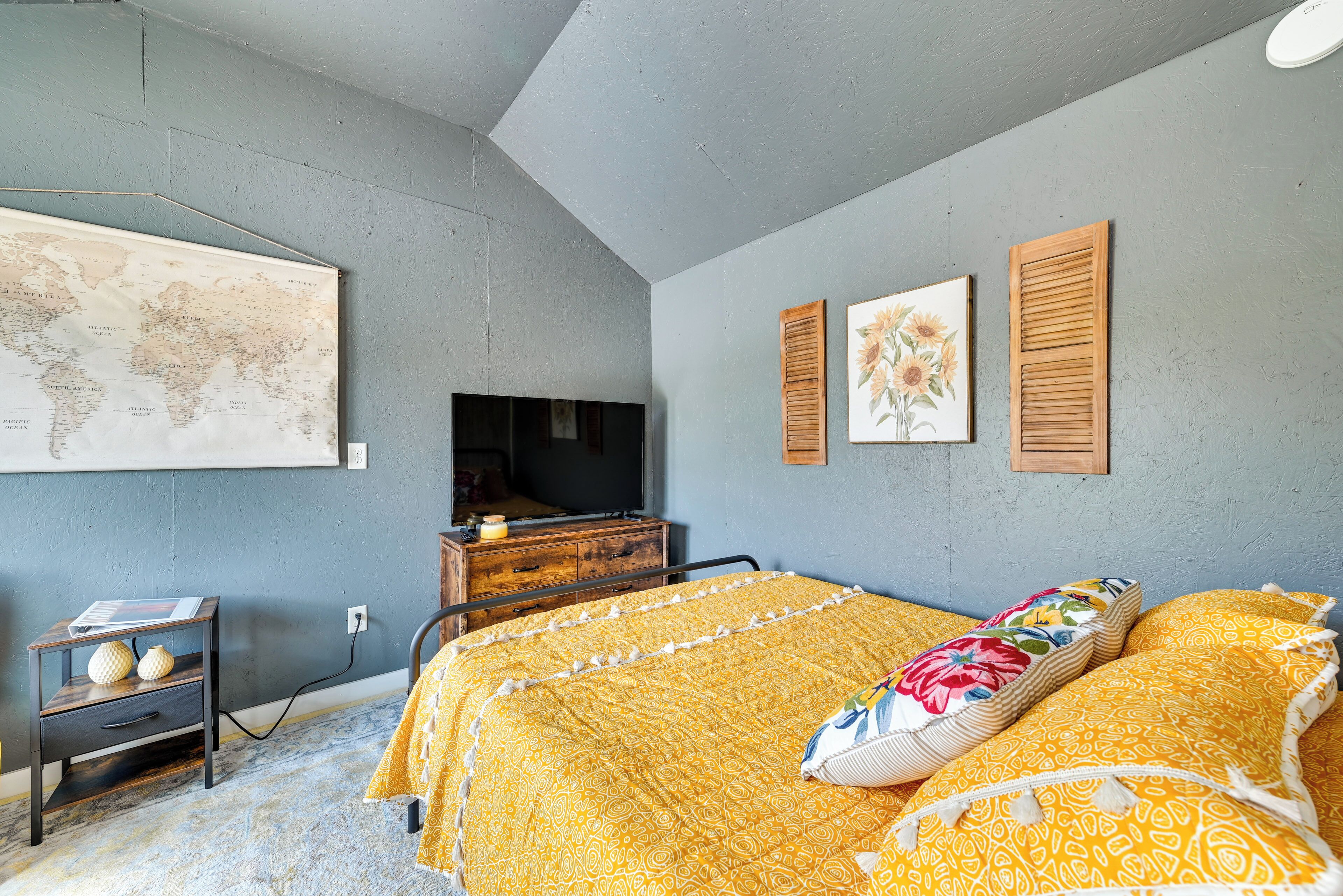 Une chambre à coucher avec un lit, une commode, une carte accrochée au mur et un téléviseur.