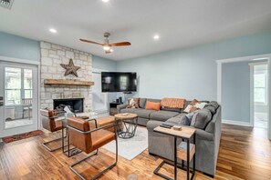 A living room with a stone fireplace, a ceiling fan, a gray sectional sofa, and a TV mounted on the wall.
