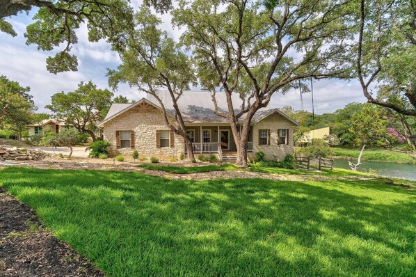 A stone house with a porch, surrounded by lush green grass and trees.