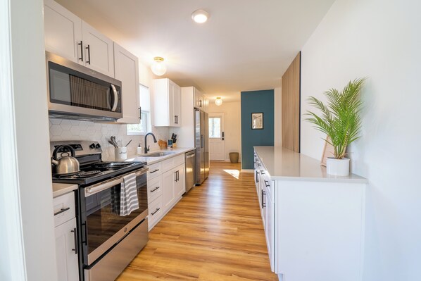 Enjoy cooking in this well-equipped kitchen with stainless steel appliances, white cabinetry, and a microwave, stove, oven, and dishwasher.