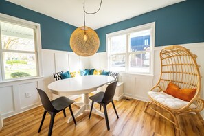 Relax in this inviting dining area with a round table and four chairs, complemented by a cozy wicker chair and a large window.