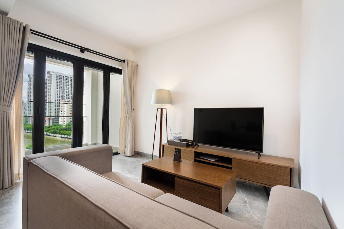 A modern hotel room with a large window, a flat-screen TV, a sofa, and a wooden coffee table.